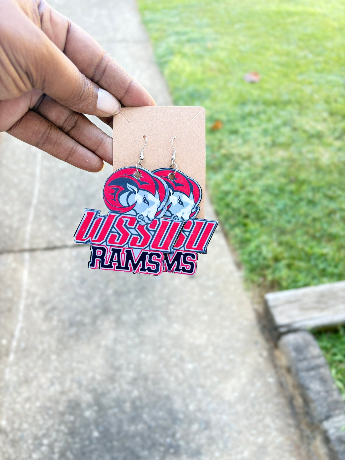 Earrings with 'Louisville Rams' logo on a card held by a hand outdoors.