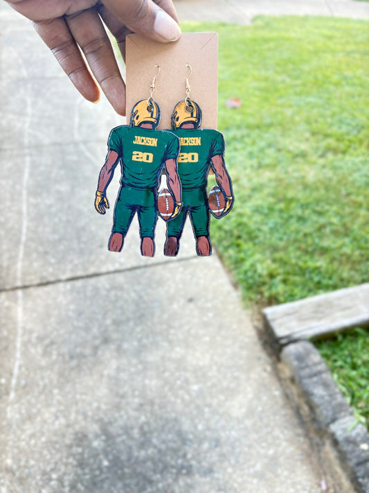 Football player earrings on a cardboard backing with a grassy background