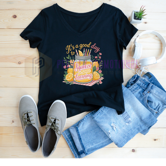 Black t-shirt with a colorful graphic and text, paired with jeans and sneakers on a wooden surface.